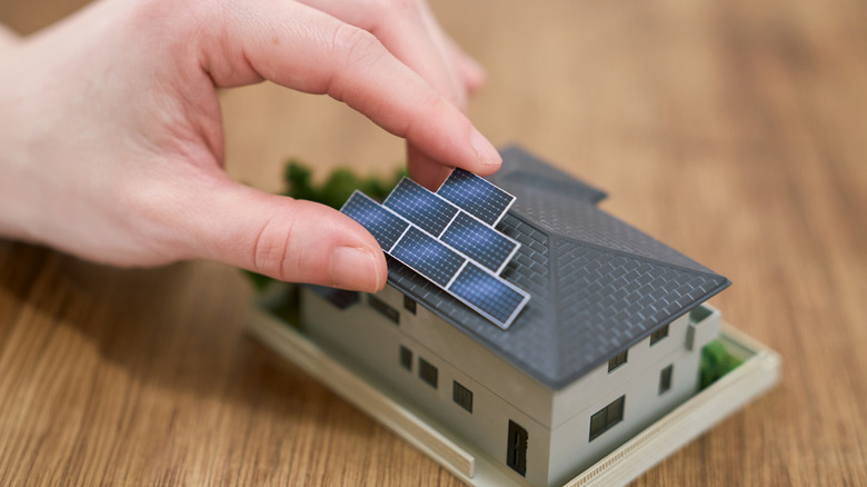 A hand installing tiny solar panels on a miniature home