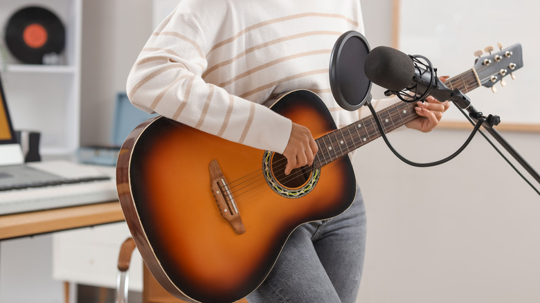 A woman recording her guitar playing with a mic