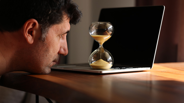 Man staring at an hourglass waiting for time to pass