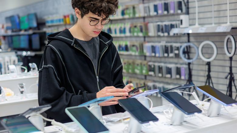 Young man in an electronics store near a phone display