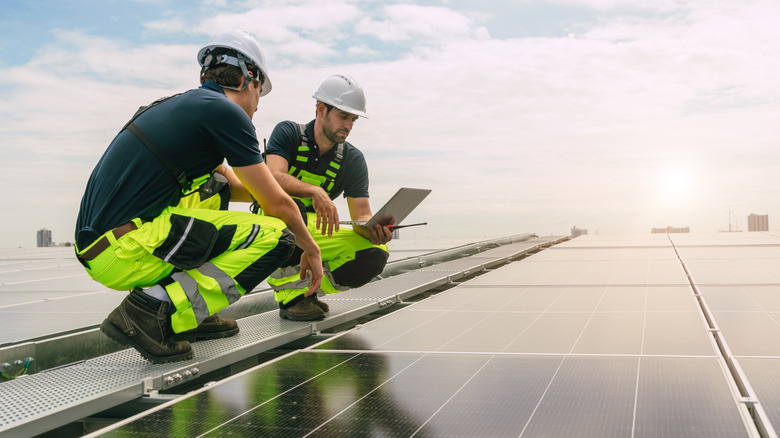 Engineers installing and checking solar panels on a large building's roof.