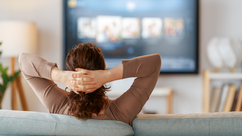 Woman sitting on sofa watching projector screen on other side of room
