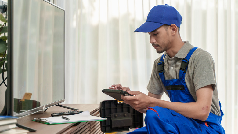 A TV technician using an external device to diagnose a TV in a living room.