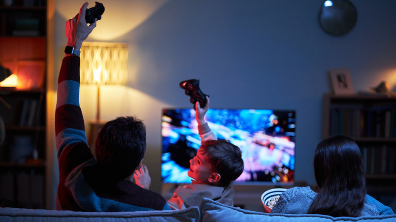 a family sitting on a couch while doing console gaming and holding hands up high with a controller