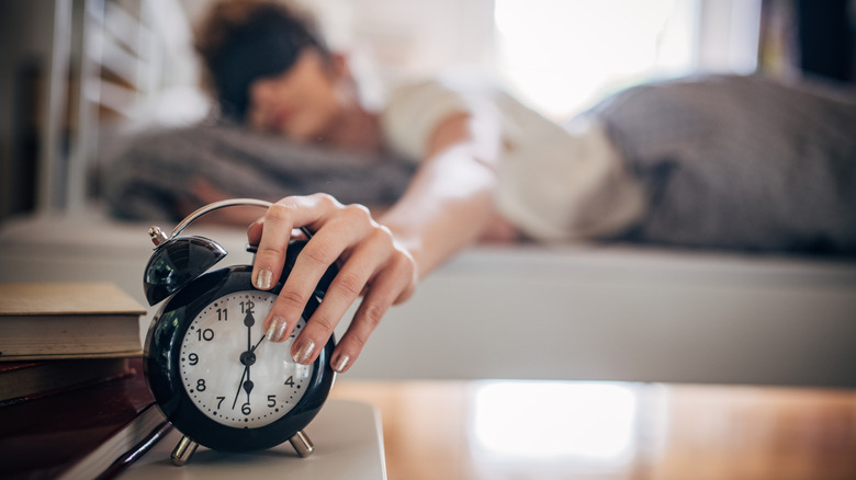 A person reaching for an alarm clock from their bed.