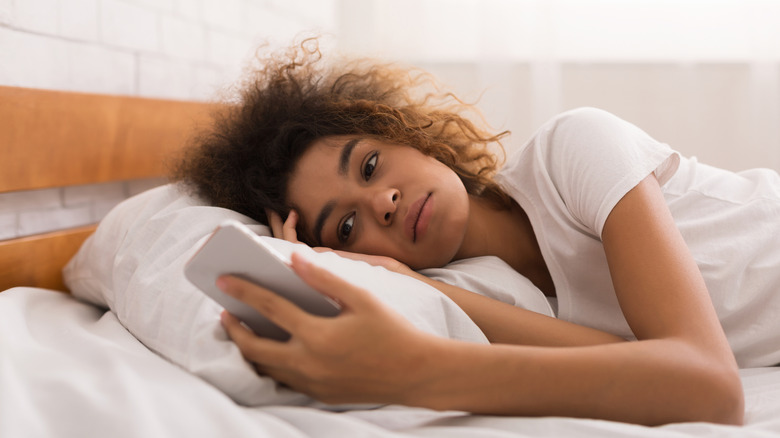 A woman looking at a phone in bed.