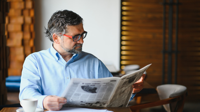 A man reading a newspaper at a table.
