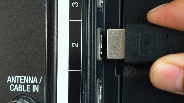 A hand plugging in an HDMI cable to the back of a TV