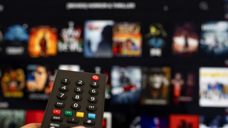 A person points a remote at a blurred TV background of apps.