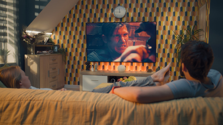 A couple sitting on a couch watching an action movie.