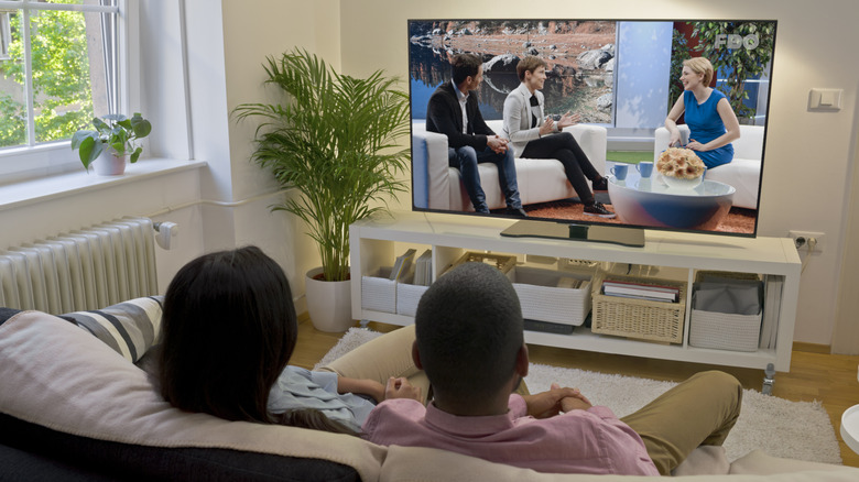 A couple sitting on a couch watching a talk show on TV.