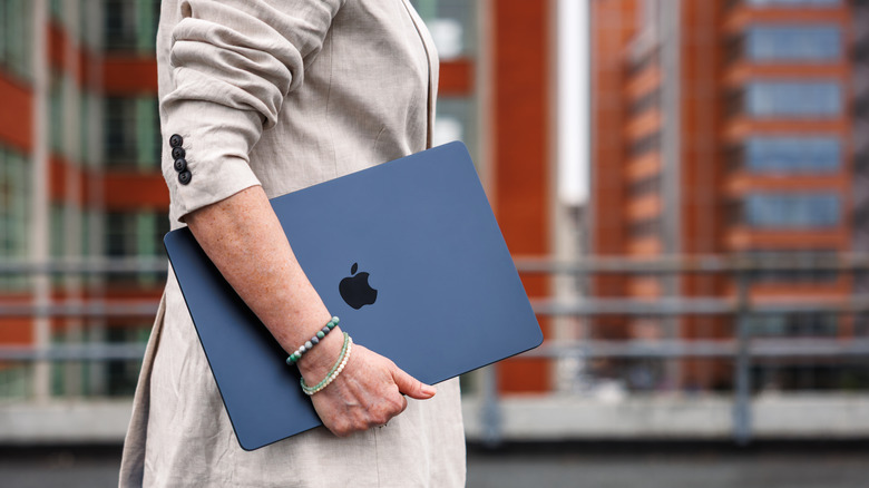 A person holding a MacBook as they walk down a city street.