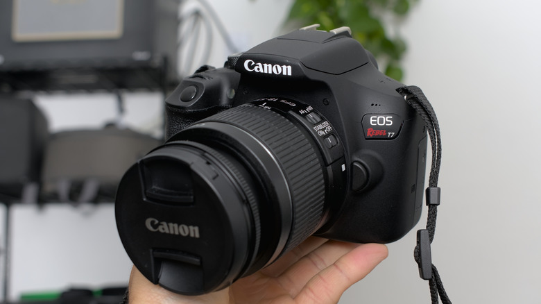 A person holds up a Canon EOS Rebel T7 camera