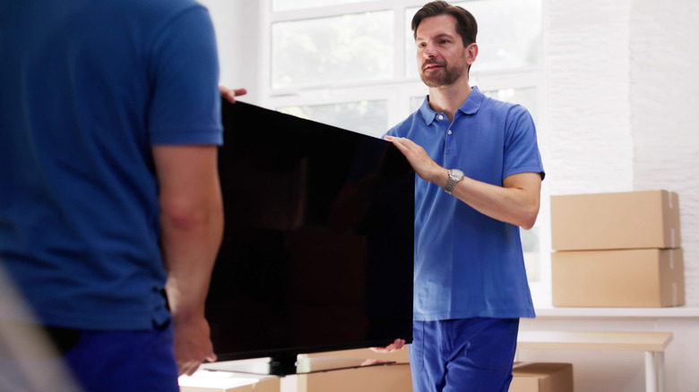Two men holding and moving a TV that's off with boxes nearby.