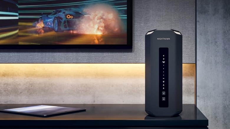 A NETGEAR WiFi 7 Router Nighthawk Tri-Band WiFi 7 (RS700S) on a media unit with a racing game on the TV.