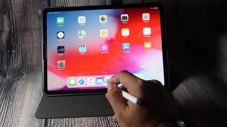 A hand selecting an icon on an Apple iPad using the Apple Pencil Pro.
