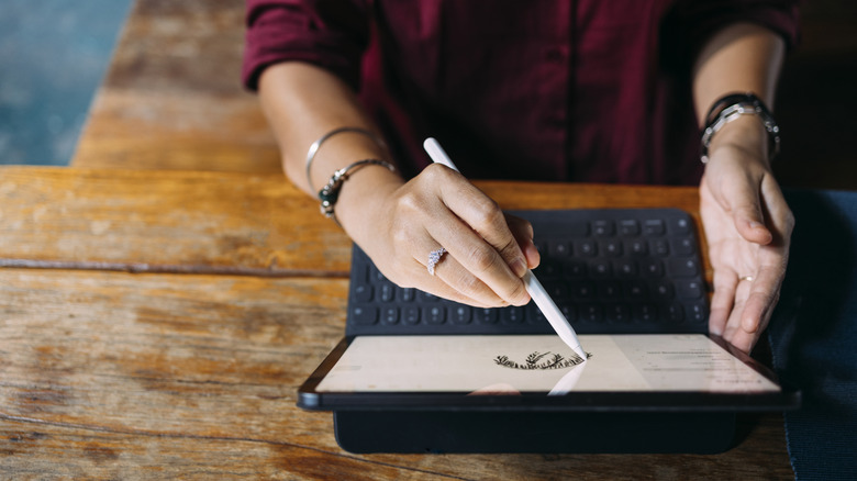 An overhead view of a woman using a stylus on a tablet.