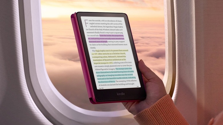 A hand holding a Kindle Colorsoft with colored highlighting on book by an airplane window
