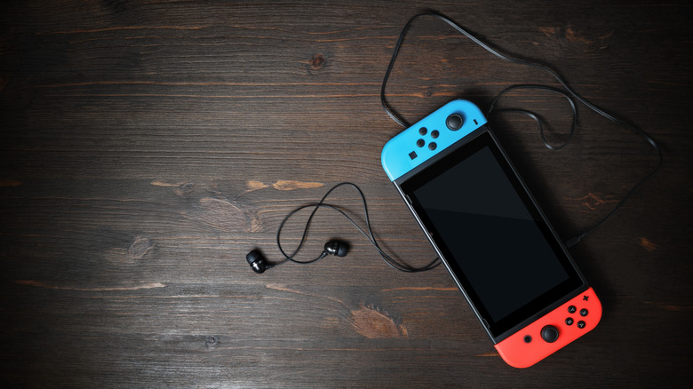 A Nintendo Switch with a pair of black earphones on wood