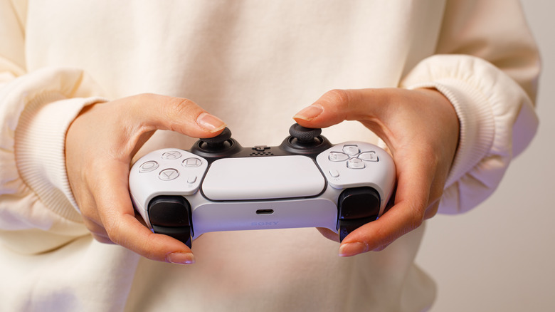Woman wearing white sweater holding PlayStation 5 DualSense controller