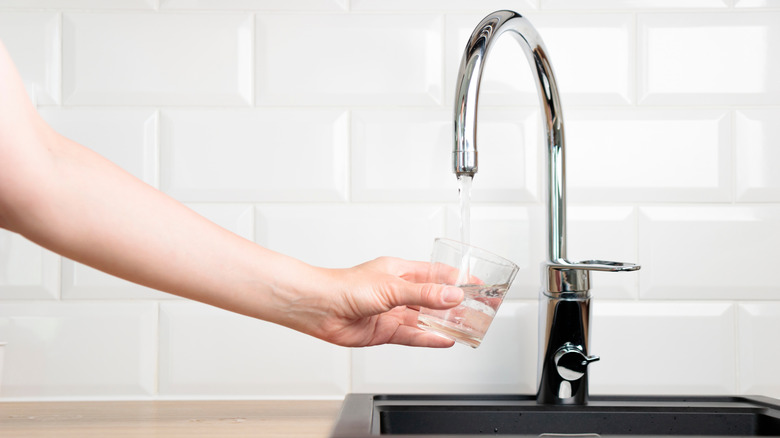 a person's hand filling up a glass of water from a faucet