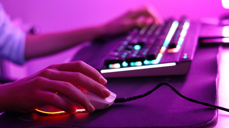 Close-up of someone using an RGB-illuminated gaming mouse and keyboard combo at their desk.