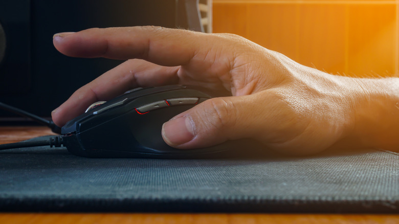 A user with their hand on a gaming mouse with RGB and side buttons.