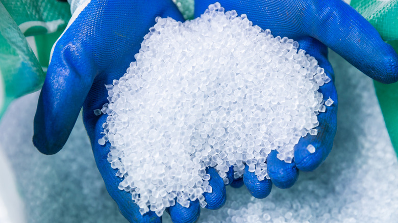 A person wearing gloves holding up pellets made of recycled plastic.