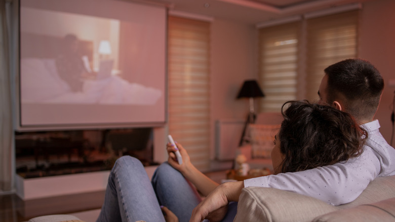 Couple on a couch watching a projector screen in view and in use.