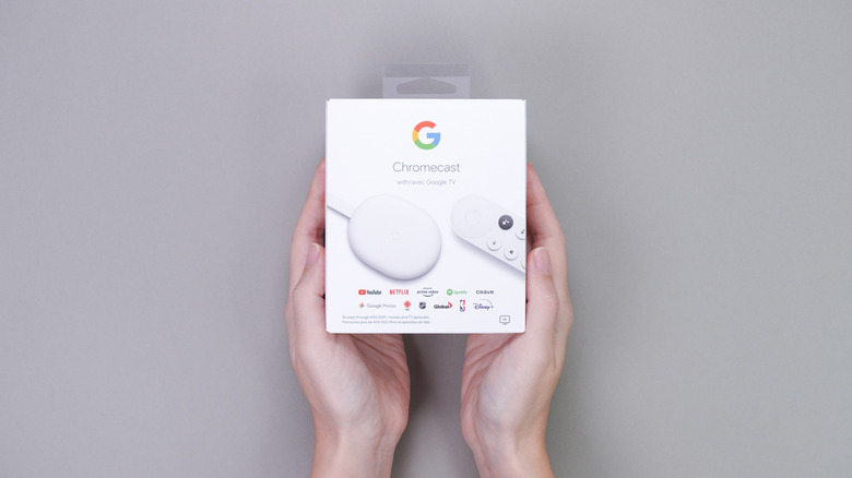 Two hands holding a Chromecast with Google TV inside its packaging.