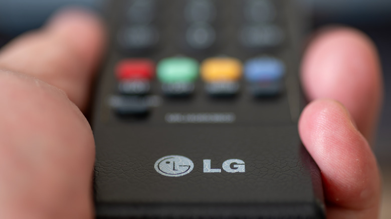 A close-up of a hand holding an LG TV remote.