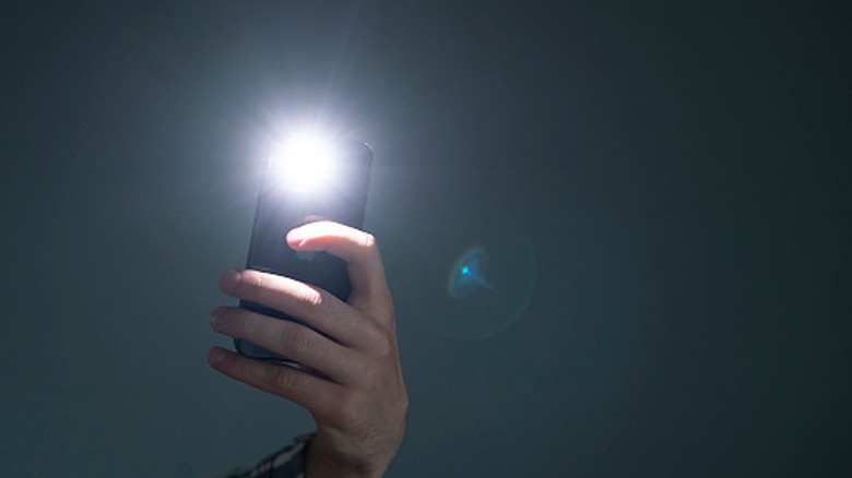 A person holding a phone with its flashlight turned on