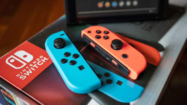 A pair of blue and red Joy-Con on top of a Nintendo Switch box with the console in the background