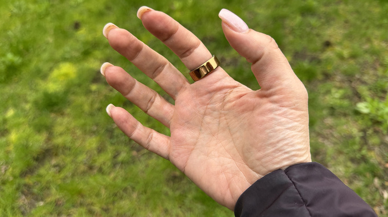 The palm side of a hand wearing an Oura Ring 4 with grass in the background.