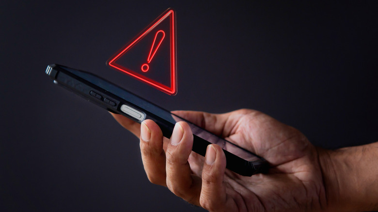 Smartphone in hand with red caution symbol above.