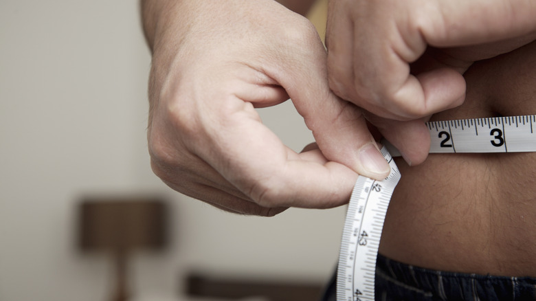 a man measuring his waistline for body fat percentage