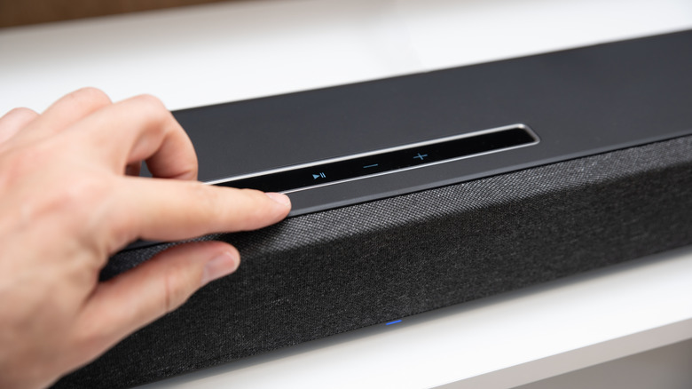 A person using the touchscreen buttons on their soundbar to control it.