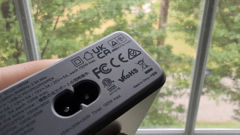 A charging brick held in front of a window, with several regulatory symbols on the brick in focus