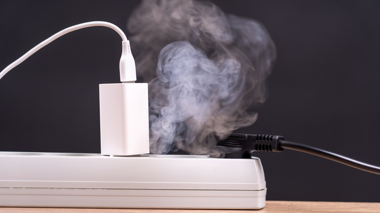 A charger and a power cable plugged into a power strip, with smoke rising from the power strip.