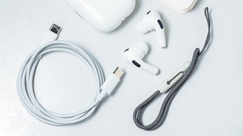 AirPods Pro 2 on a table between the charging case, USB-C charging cable, and a lanyard strap.