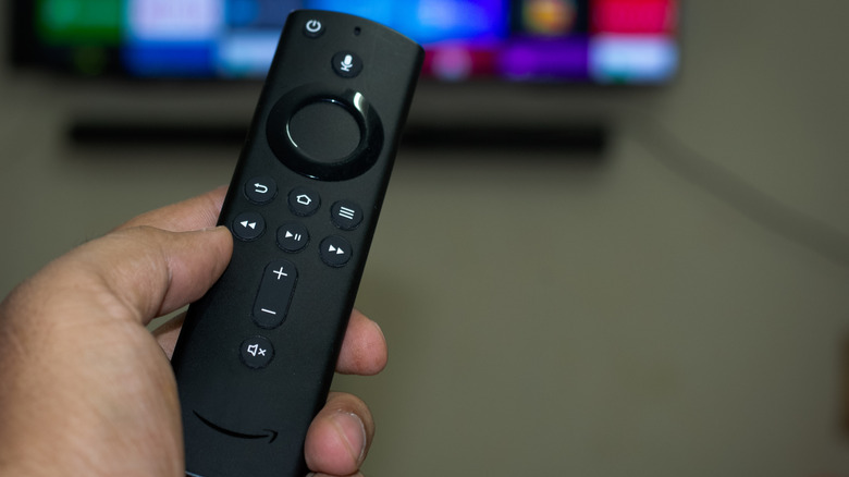 A person holding a Fire TV remote in front of a wall-mounted TV.