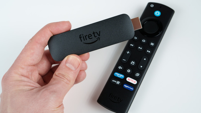 A person holding an Amazon Fire TV Stick in front of an Alexa Voice Remote.