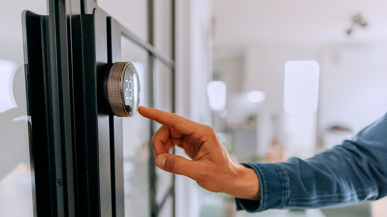 Man adjusting a smart thermostat on a wall inside a home