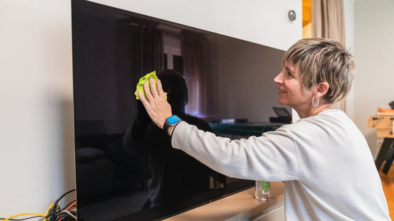 A woman cleaning a TV with a microfiber cloth.