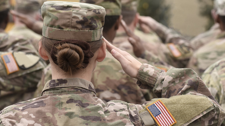 the back of a female soldier in a group of US military soldiers saluting