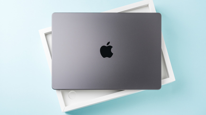 A silver MacBook sitting on top of its white packaging -- these items sit against a blue backdrop