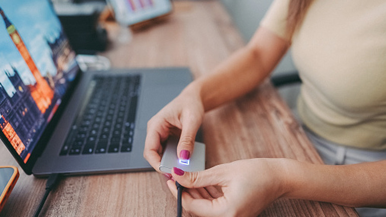 A person plugging an external SSD into a laptop via USB.