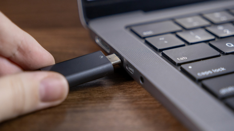 Hand inserting a USB Type-C-compatible flash drive into a laptop port.