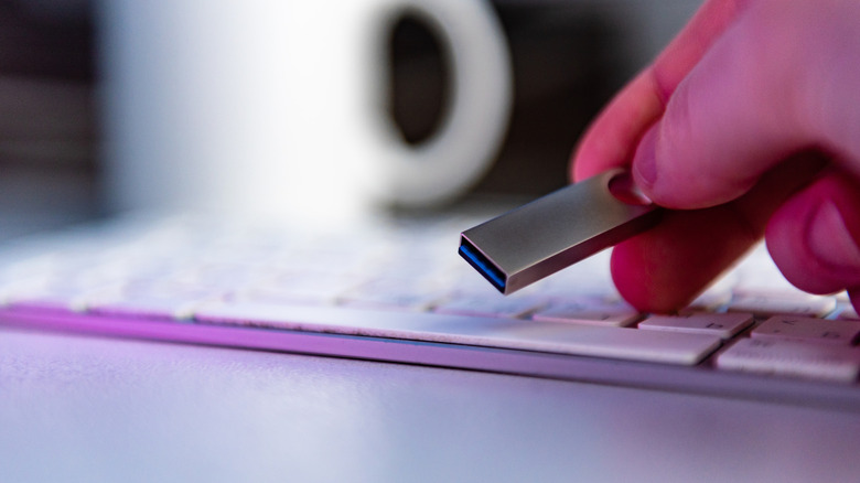 Hand holding a slim USB flash drive above a keyboard.