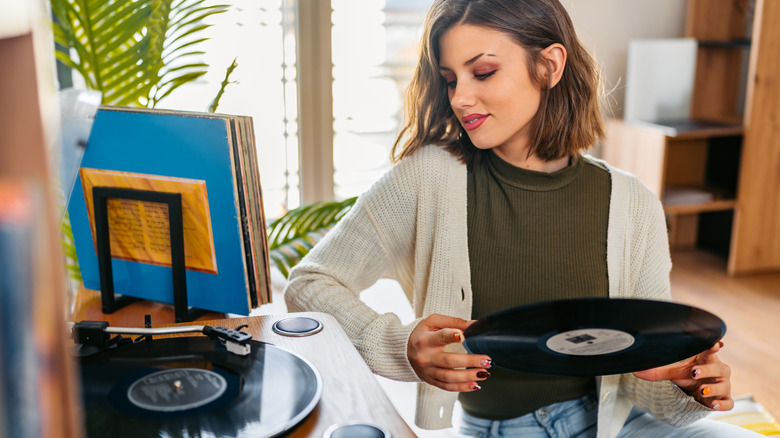 Person holding a record and looking at a record player